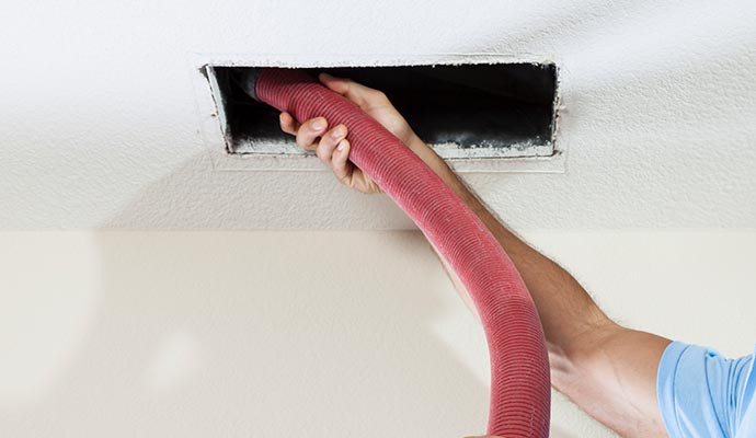 Person cleaning an air duct with a vacuum hose