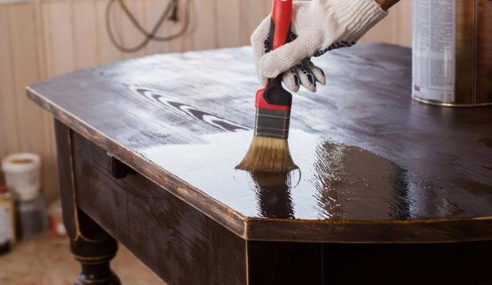 Person applying varnish to a wooden table with equipment