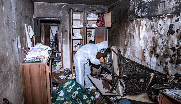 Person in protective gear cleaning a fire-damaged room