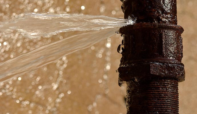 old, rusty metal pipe with water spraying out from a break